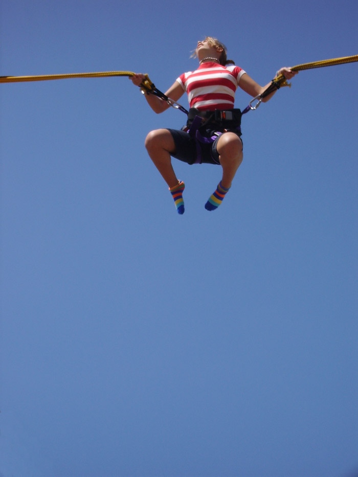 A young woman bounces high up into the air restrained by a harness