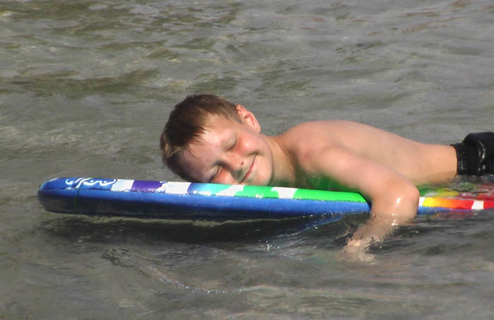 Tim lies smiling on a surf board on the ocean in the sun