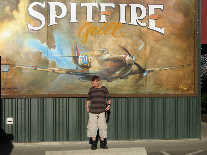 Tim 'wincing' while standing in front of a painting of a huge Spitfire which is flying towards him.