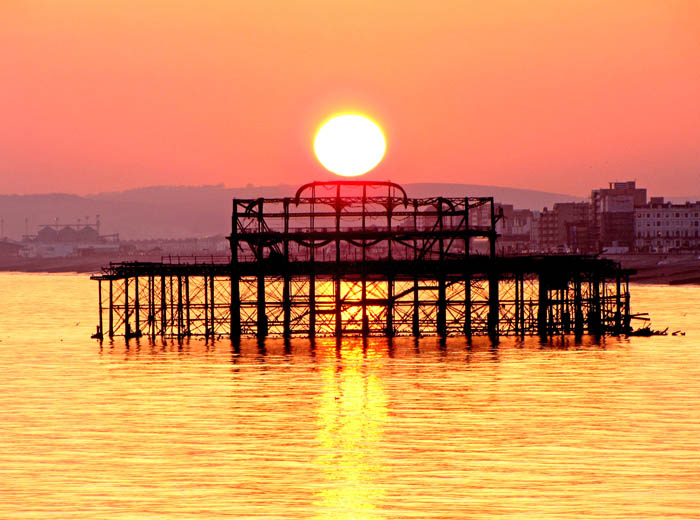 A photo of a sunset on a beach with the skeleton of a pier.